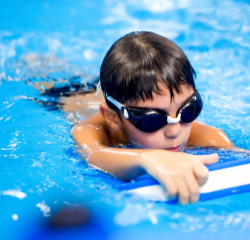 Boy paddling on kick board in swimming pool at Water Champs class